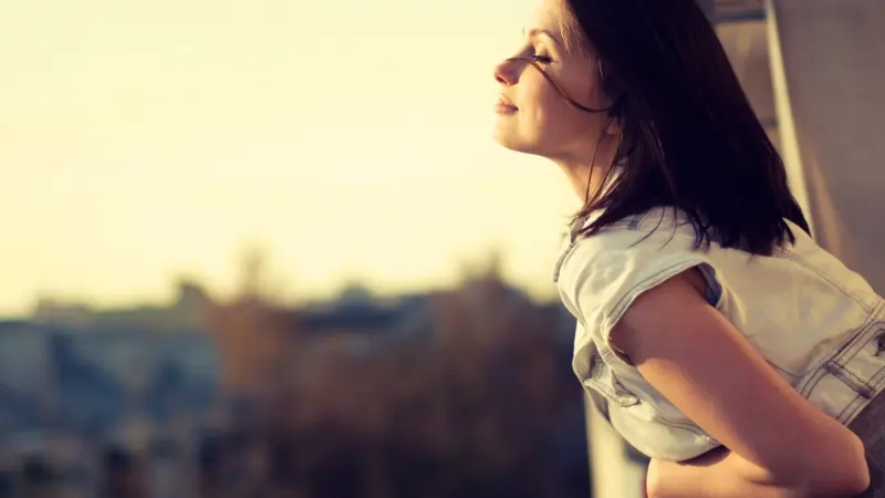 Woman leaning forward outdoors with eyes closed, enjoying the breeze and sunlight.