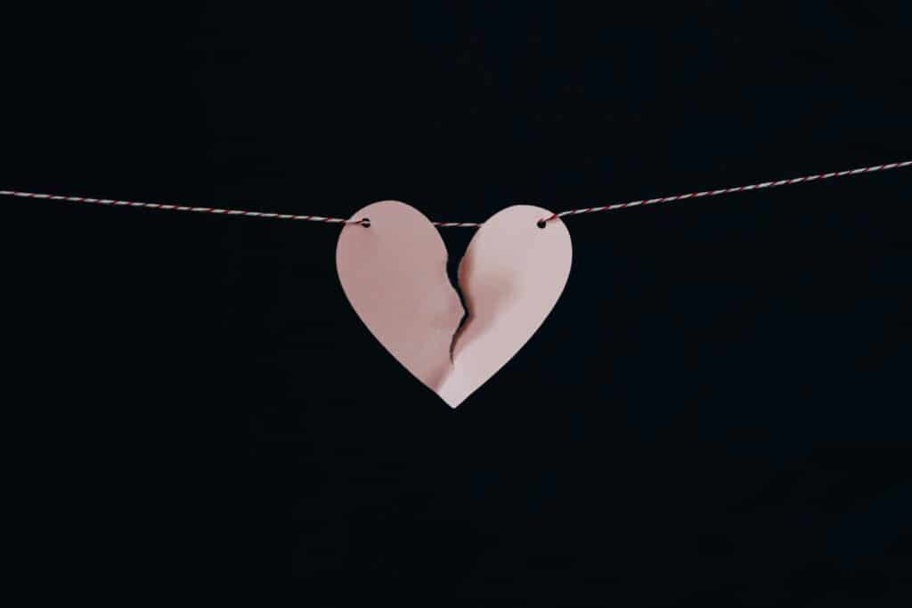 A torn pink paper heart hanging on a string against a black background.