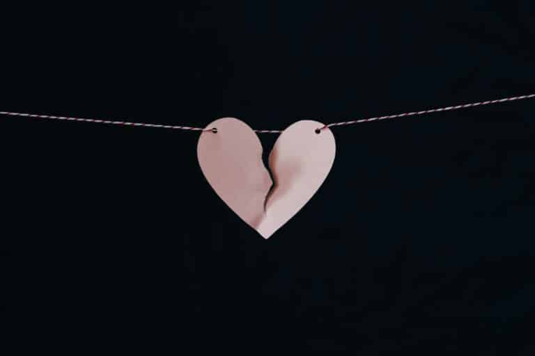 A torn pink paper heart hanging on a string against a black background.