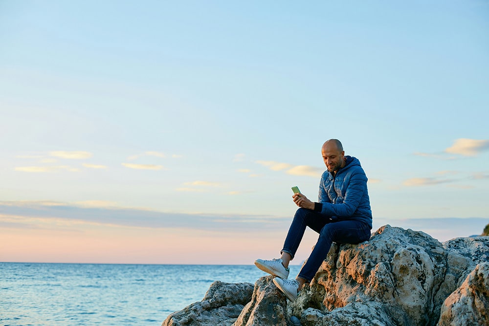 A young man standing on the beach with the sea in the background.